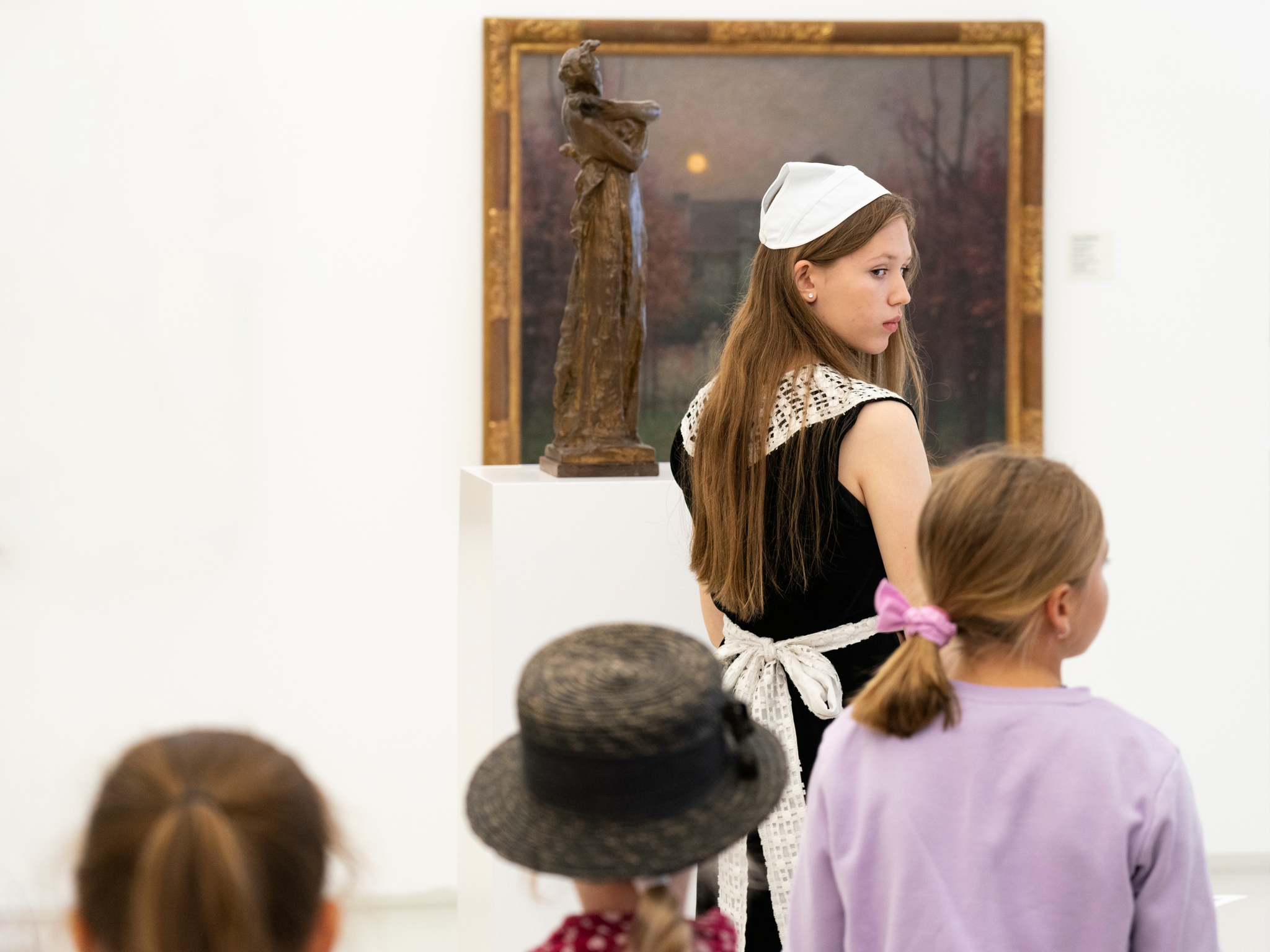 Dívka před obrazem, která se otáčí na zvědavě pozorující děti - fotografie z edukačního programu Záhada smutné dívky